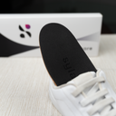 A SYLACORE insole inserted into a white sneaker, viewed from the side, with its packaging in the background